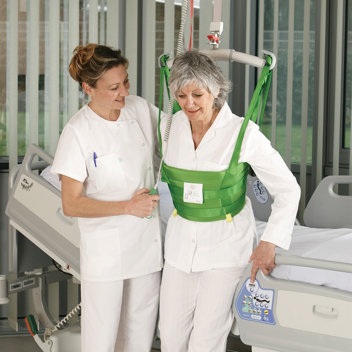 Klinicystka pomaga pacjentce podczas stanąć na nogi w szpitalu przy użyciu podnośnika sufitowego i kamizelki do podnoszenia MasterVest